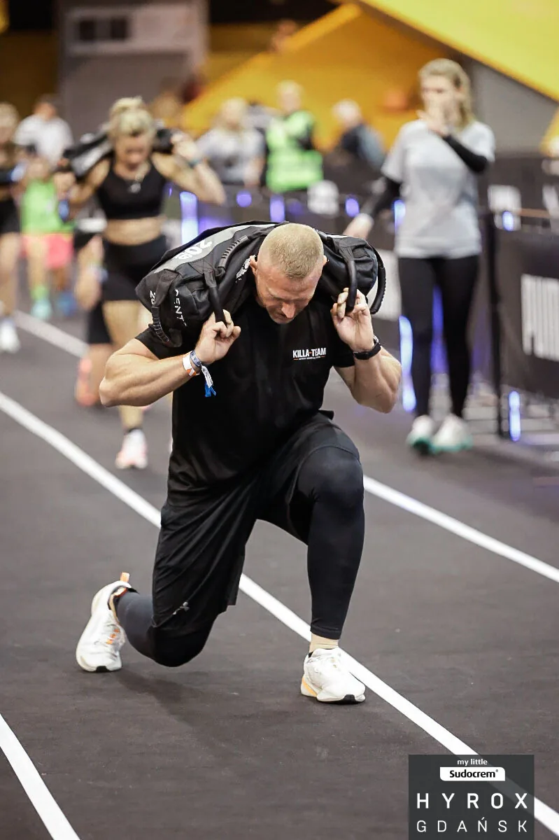 Jakub Kaszuba robi wykroki z workiem na zawodach HYROX Gdańsk 2026